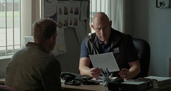 Movie still from “Sorry We Missed You” (2019), directed by Ken Loach – A man sitting at a table with a paper in front of him; Medium shot, Over the shoulder angle