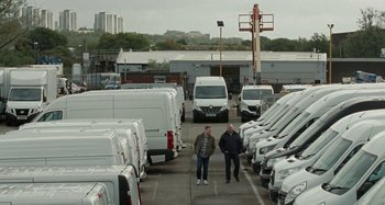 Movie still from “Sorry We Missed You” (2019), directed by Ken Loach – Two men are walking through a parking lot full of white vans; Extreme Wide shot, High angle
