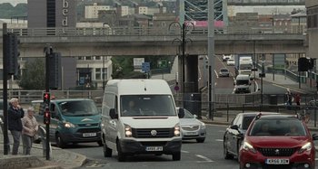 Movie still from “Sorry We Missed You” (2019), directed by Ken Loach – A white van driving down a street next to a bridge; Extreme Wide shot, Over the shoulder angle