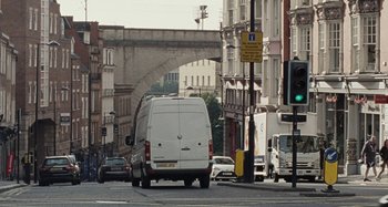 Movie still from “Sorry We Missed You” (2019), directed by Ken Loach – A white van driving down a street next to tall buildings; Extreme Wide shot, High angle