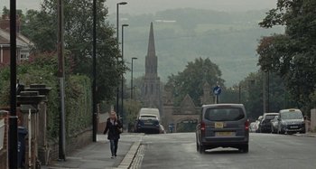 Movie still from “Sorry We Missed You” (2019), directed by Ken Loach – A woman walking down a street with cars in the background; Extreme Wide shot, High angle
