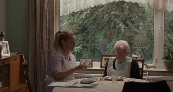 Movie still from “Sorry We Missed You” (2019), directed by Ken Loach – An older woman sitting at a table with an older woman holding a picture; Medium shot, Over the shoulder angle
