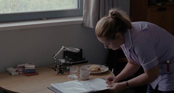 Movie still from “Sorry We Missed You” (2019), directed by Ken Loach – A woman is writing on a book on a table; Medium shot, High angle