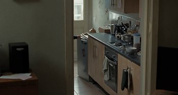 Movie still from “Sorry We Missed You” (2019), directed by Ken Loach – A cluttered kitchen with a trash can and a garbage can; Medium shot, High angle