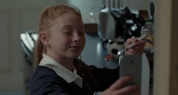 Movie still from “Sorry We Missed You” (2019), directed by Ken Loach – A young girl eating food while looking at a cell phone; Close Up shot, Over the shoulder angle