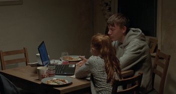 Movie still from “Sorry We Missed You” (2019), directed by Ken Loach – A boy and a little girl sitting at a dinner table looking at a computer; Medium shot, Over the shoulder angle