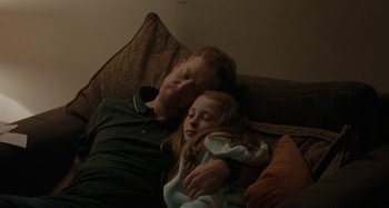 Movie still from “Sorry We Missed You” (2019), directed by Ken Loach – A man and a little girl are sleeping on a couch; Medium shot, High angle