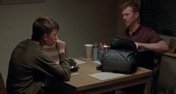Movie still from “Sorry We Missed You” (2019), directed by Ken Loach – Two people sitting at a table with a backpack; Medium shot, Over the shoulder angle