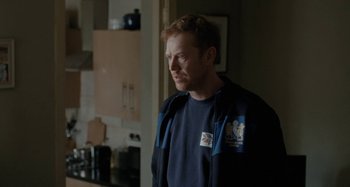 Movie still from “Sorry We Missed You” (2019), directed by Ken Loach – A man standing in a kitchen looking to his left; Medium shot, Over the shoulder angle