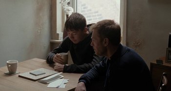 Movie still from “Sorry We Missed You” (2019), directed by Ken Loach – Two young men sitting at a table drinking coffee; Medium shot, Over the shoulder angle