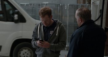 Movie still from “Sorry We Missed You” (2019), directed by Ken Loach – A man standing next to another man while looking at a cell phone; Medium shot, Over the shoulder angle