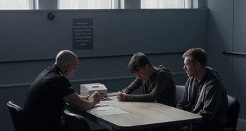 Movie still from “Sorry We Missed You” (2019), directed by Ken Loach – Three people sitting at a table with papers on the table; Medium shot, Over the shoulder angle