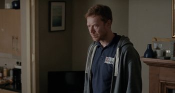 Movie still from “Sorry We Missed You” (2019), directed by Ken Loach – A man in a blue shirt and a gray jacket; Medium shot, Over the shoulder angle