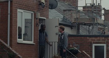 Movie still from “Sorry We Missed You” (2019), directed by Ken Loach – Two men standing outside of a building talking; Wide shot, Over the shoulder angle