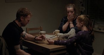 Movie still from “Sorry We Missed You” (2019), directed by Ken Loach – A group of people sitting at a wooden table; Medium shot, High angle
