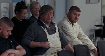 Movie still from “Sorry We Missed You” (2019), directed by Ken Loach – A group of people sitting next to each other in a room; Medium shot, High angle