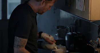 Movie still from “Sorry We Missed You” (2019), directed by Ken Loach – A man in a black t - shirt is putting something in a cup; Medium shot, Over the shoulder angle