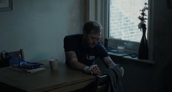 Movie still from “Sorry We Missed You” (2019), directed by Ken Loach – A man sitting at a table with a cup of coffee in front of him; Medium shot, Over the shoulder angle