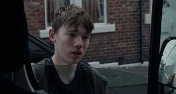 Movie still from “Sorry We Missed You” (2019), directed by Ken Loach – A young man standing in front of a brick building; Close Up shot, Over the shoulder angle