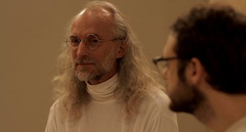 Movie still from “Sound of My Voice” (2011), directed by Zal Batmanglij – An older man with long hair and glasses is looking at a younger man; Close Up shot, Over the shoulder angle