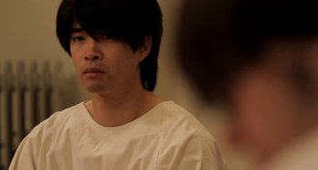Movie still from “Sound of My Voice” (2011), directed by Zal Batmanglij – A man with long black hair wearing a white t - shirt; Close Up shot, Over the shoulder angle