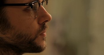 Movie still from “Sound of My Voice” (2011), directed by Zal Batmanglij – A man's face wearing glasses; Close Up shot, Over the shoulder angle
