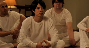 Movie still from “Sound of My Voice” (2011), directed by Zal Batmanglij – A man sitting on the ground with another man sitting on the floor; Medium shot, Over the shoulder angle