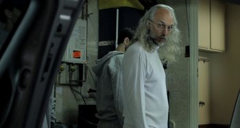 Movie still from “Sound of My Voice” (2011), directed by Zal Batmanglij – A man with long white hair and a beard standing next to another man; Medium shot, Over the shoulder angle