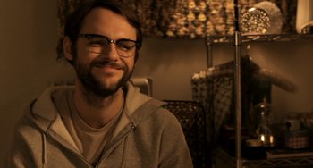 Movie still from “Sound of My Voice” (2011), directed by Zal Batmanglij – A man wearing glasses and a hoodie smiling for the camera; Close Up shot, Over the shoulder angle