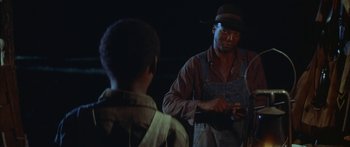 Movie still from “Sounder” (1972), directed by Martin Ritt – A man standing next to another man in a dark room; Medium shot, Over the shoulder angle