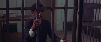 Movie still from “Sounder” (1972), directed by Martin Ritt – A man in a suit and tie behind bars; Medium shot, High angle