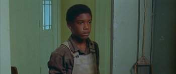 Movie still from “Sounder” (1972), directed by Martin Ritt – A young boy wearing an overalls standing in front of a door; Close Up shot, High angle