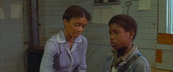 Movie still from “Sounder” (1972), directed by Martin Ritt – A woman sitting next to a young man in front of a wall; Medium shot, Over the shoulder angle