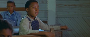 Movie still from “Sounder” (1972), directed by Martin Ritt – A young boy sitting on top of a wooden bench; Medium shot, Low angle