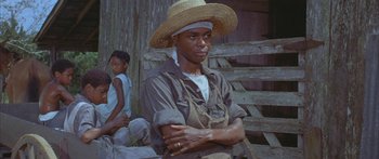 Movie still from “Sounder” (1972), directed by Martin Ritt – A man wearing a straw hat standing in front of a wooden fence; Medium shot, High angle