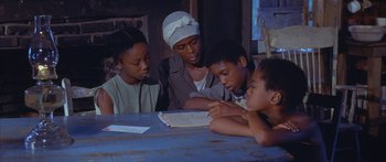 Movie still from “Sounder” (1972), directed by Martin Ritt – A group of people sitting at a table reading a book; Medium shot, High angle