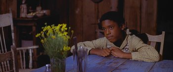 Movie still from “Sounder” (1972), directed by Martin Ritt – A young man sitting at a table with a knife and fork; Medium shot, High angle
