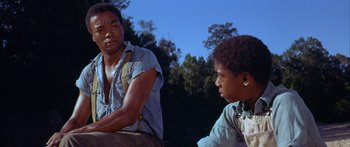Movie still from “Sounder” (1972), directed by Martin Ritt – A man sitting next to a boy in a field; Medium shot, Low angle
