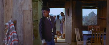 Movie still from “Sounder” (1972), directed by Martin Ritt – A man in a suit and tie standing in front of a door; Medium shot, Low angle