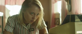 Movie still from “Southbound” (2015), directed by Tyler Gillett – A woman sitting at a table looking at the camera; Close Up shot, Low angle