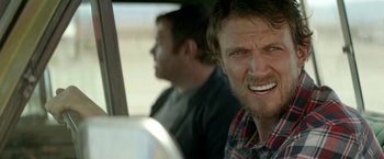 Movie still from “Southbound” (2015), directed by Tyler Gillett – A man sitting in a car with another man in the background; Close Up shot, Over the shoulder angle
