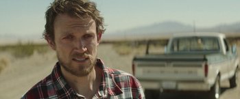 Movie still from “Southbound” (2015), directed by Tyler Gillett – A person wearing a plaid shirt near a truck; Close Up shot, Over the shoulder angle