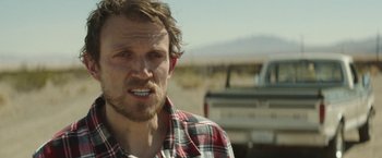 Movie still from “Southbound” (2015), directed by Tyler Gillett – A person wearing a plaid shirt near a truck; Close Up shot, Over the shoulder angle