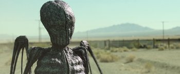 Movie still from “Southbound” (2015), directed by Tyler Gillett – A statue of a person holding a stick in the desert; Medium shot, Low angle