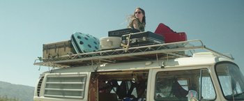 Movie still from “Southbound” (2015), directed by Tyler Gillett – A woman standing on top of a van with luggage; Wide shot, Low angle