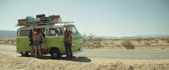 Movie still from “Southbound” (2015), directed by Tyler Gillett – A woman standing next to a green van on a dirt road; Wide shot, Low angle