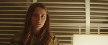 Movie still from “Southbound” (2015), directed by Tyler Gillett – A woman with long brown hair wearing a camouflage shirt; Close Up shot, Over the shoulder angle