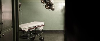 Movie still from “Southbound” (2015), directed by Tyler Gillett – A hospital bed in a room next to a green wall; Wide shot, Overhead angle