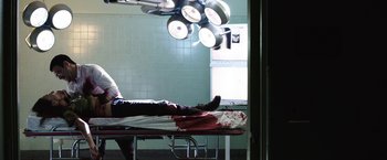 Movie still from “Southbound” (2015), directed by Tyler Gillett – A person laying on a bed in a room with lights on; Wide shot, Low angle