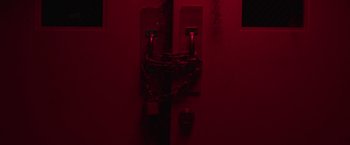 Movie still from “Southbound” (2015), directed by Tyler Gillett – A dark room with a red light on the wall; Extreme Close Up shot, High angle